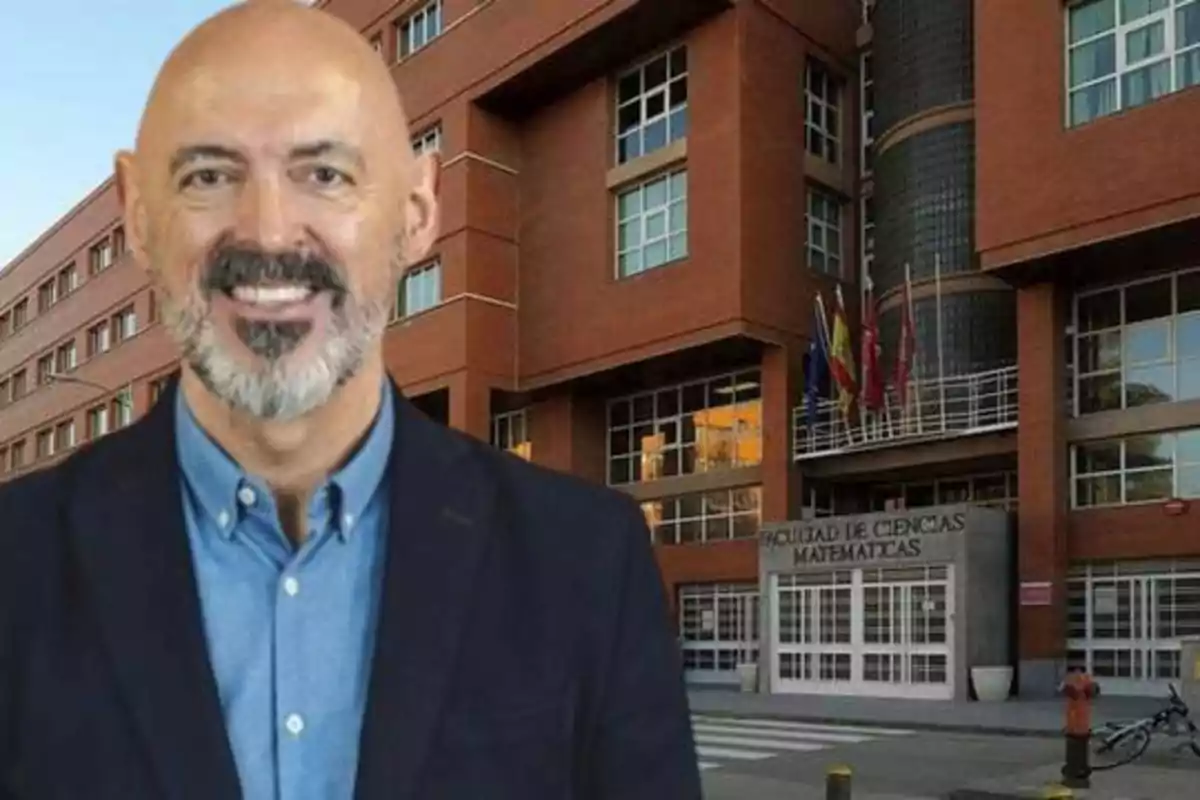 Un hombre calvo con barba sonríe frente a un edificio de ladrillo rojo con un cartel que dice "Facultad de Ciencias Matemáticas".