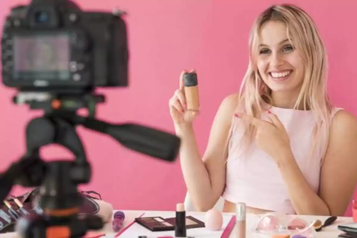 Persona sonriendo y mostrando un producto de maquillaje frente a una cámara en un entorno de grabación.