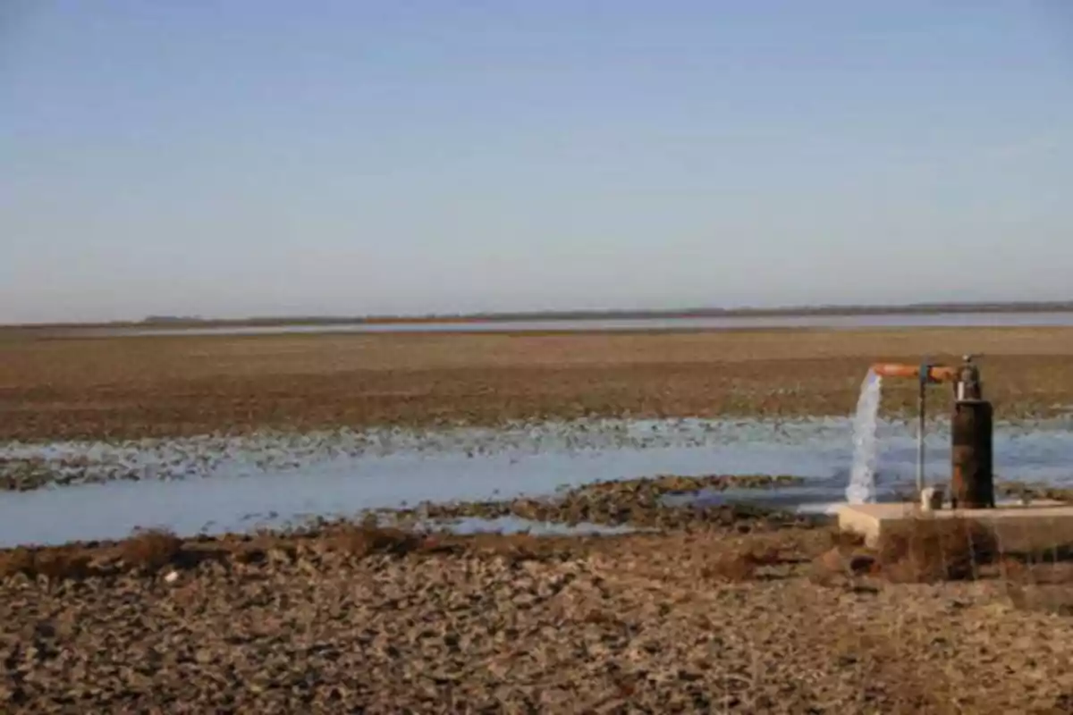 Una bomba de agua en funcionamiento en un paisaje árido con un cuerpo de agua en el fondo.