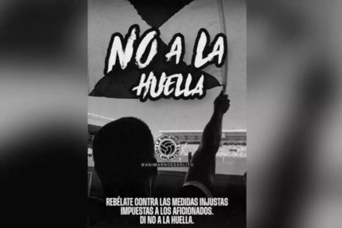 Un aficionado sostiene una bandera con el texto "NO A LA HUELGA" en un estadio, acompañado del mensaje "REBÉLATE CONTRA LAS MEDIDAS INJUSTAS IMPUESTAS A LOS AFICIONADOS. DI NO A LA HUELGA."