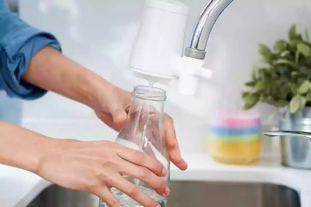 Una persona llenando una botella de vidrio con agua de un grifo que tiene un filtro.