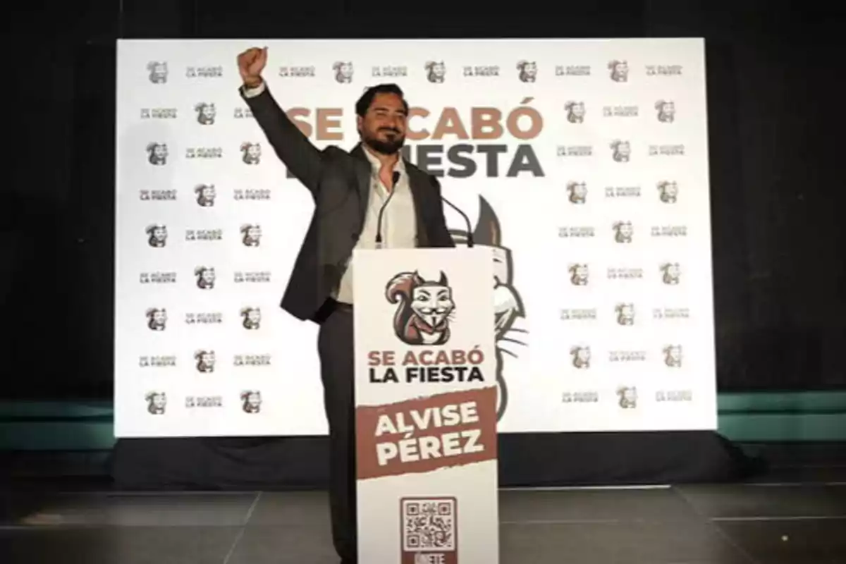 Un hombre de traje levanta el puño en un escenario con un podio que tiene un cartel que dice "Se acabó la fiesta" y "Alvise Pérez".