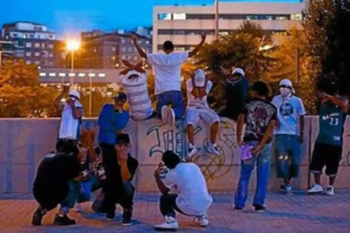 Un grupo de jóvenes posando en una plaza urbana al atardecer con edificios y luces de la ciudad al fondo.