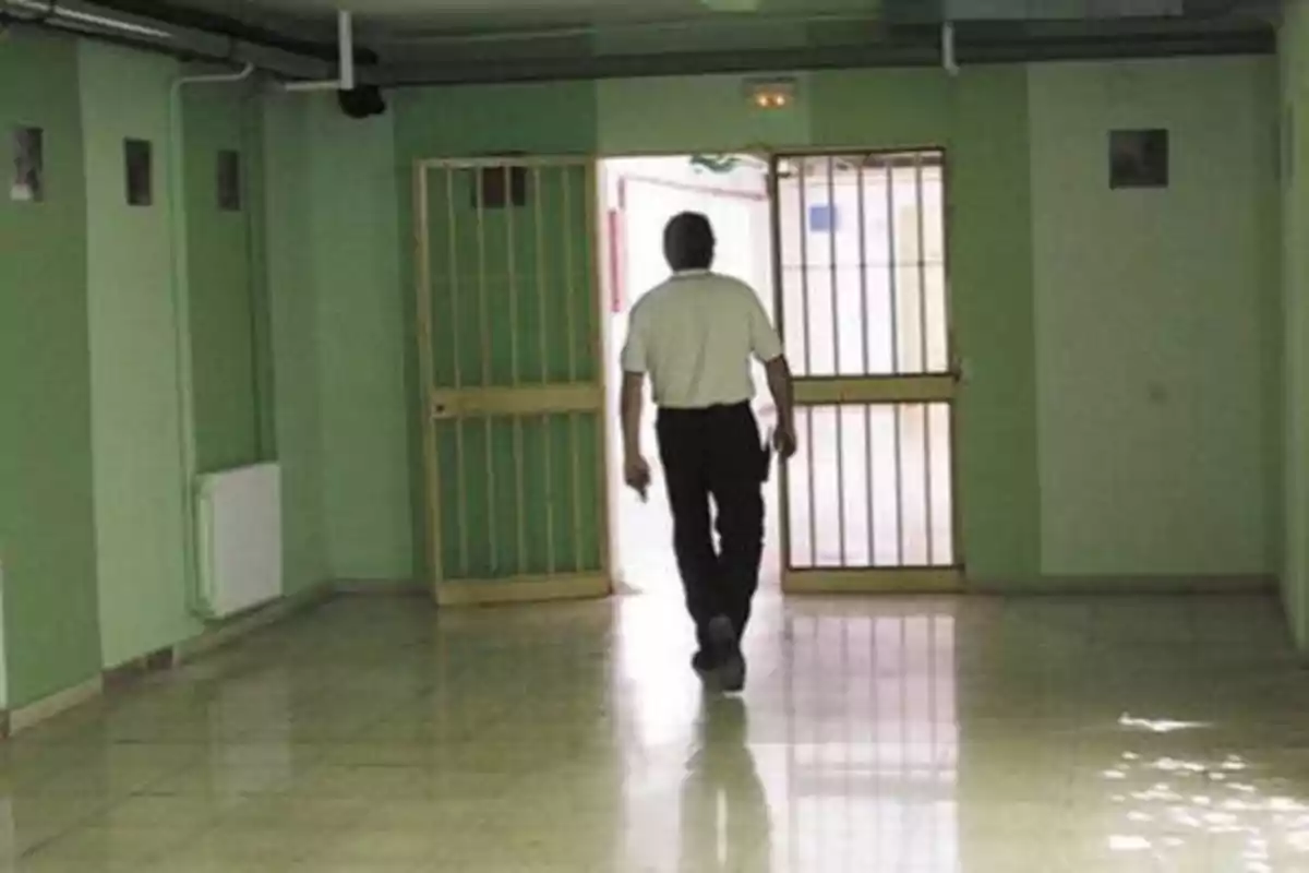 Un hombre caminando por un pasillo hacia una puerta con rejas.