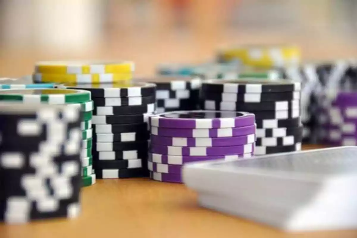 Fichas de póker de varios colores apiladas sobre una mesa junto a una baraja de cartas.