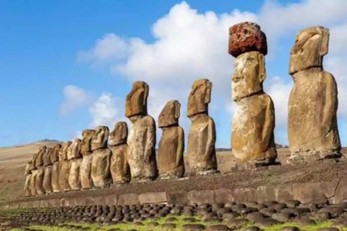 Estatuas Moái alineadas en la Isla de Pascua bajo un cielo azul con algunas nubes.