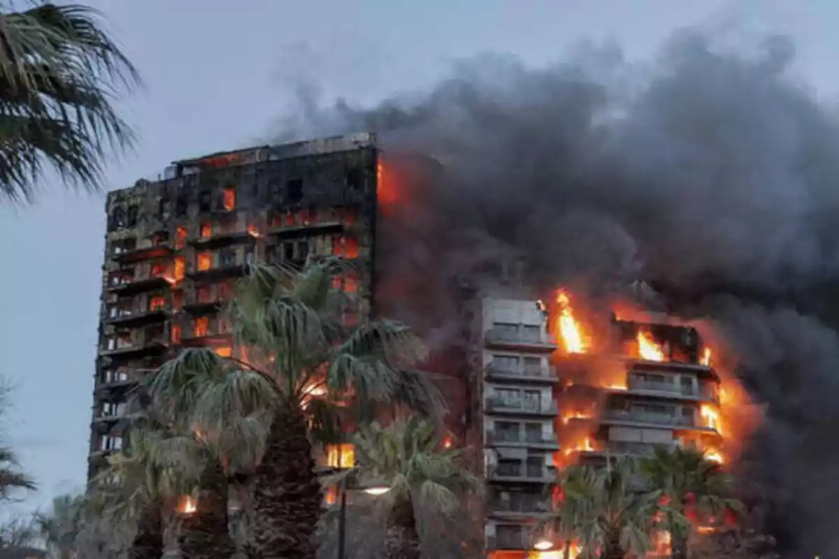 Edificio en llamas con humo negro denso saliendo de las ventanas y palmeras en primer plano.
