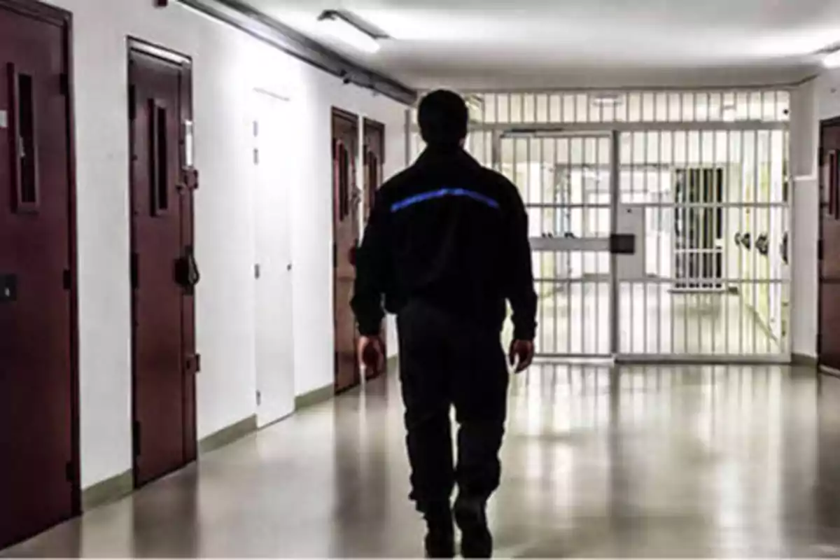 Un guardia caminando por un pasillo de una prisión con celdas a los lados.
