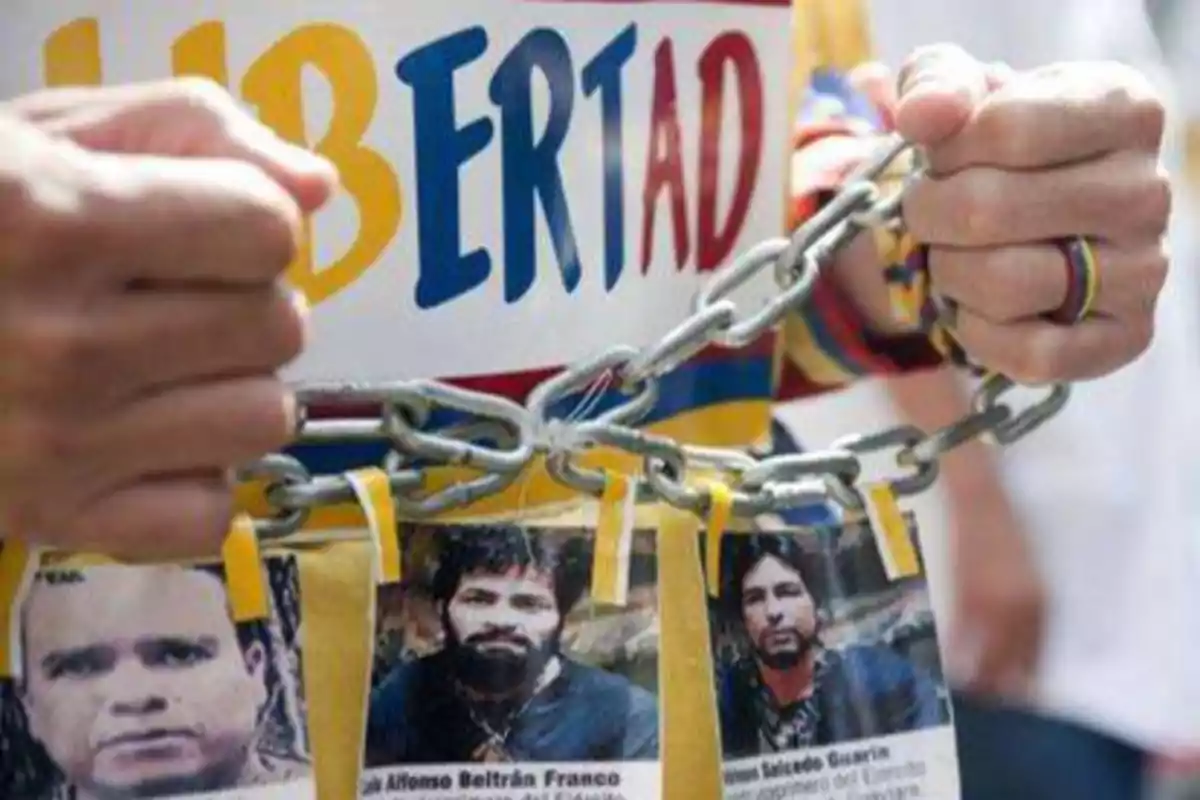 Manos encadenadas sosteniendo un cartel con la palabra "Libertad" y fotos de personas.