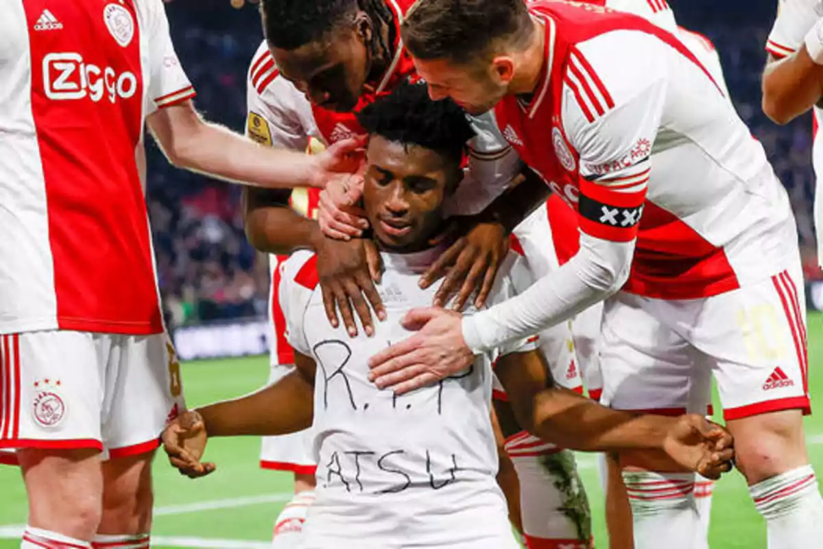 Jugadores de fútbol del Ajax abrazan a un compañero que lleva una camiseta con el mensaje "R.I.P. ATSU".