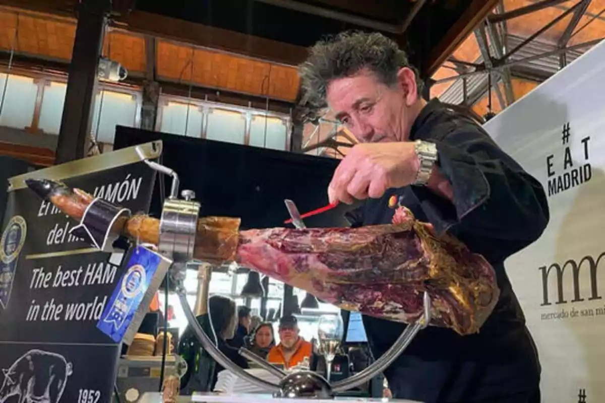 Un hombre corta jamón en un mercado de Madrid, con un cartel que dice "El mejor jamón del mundo".