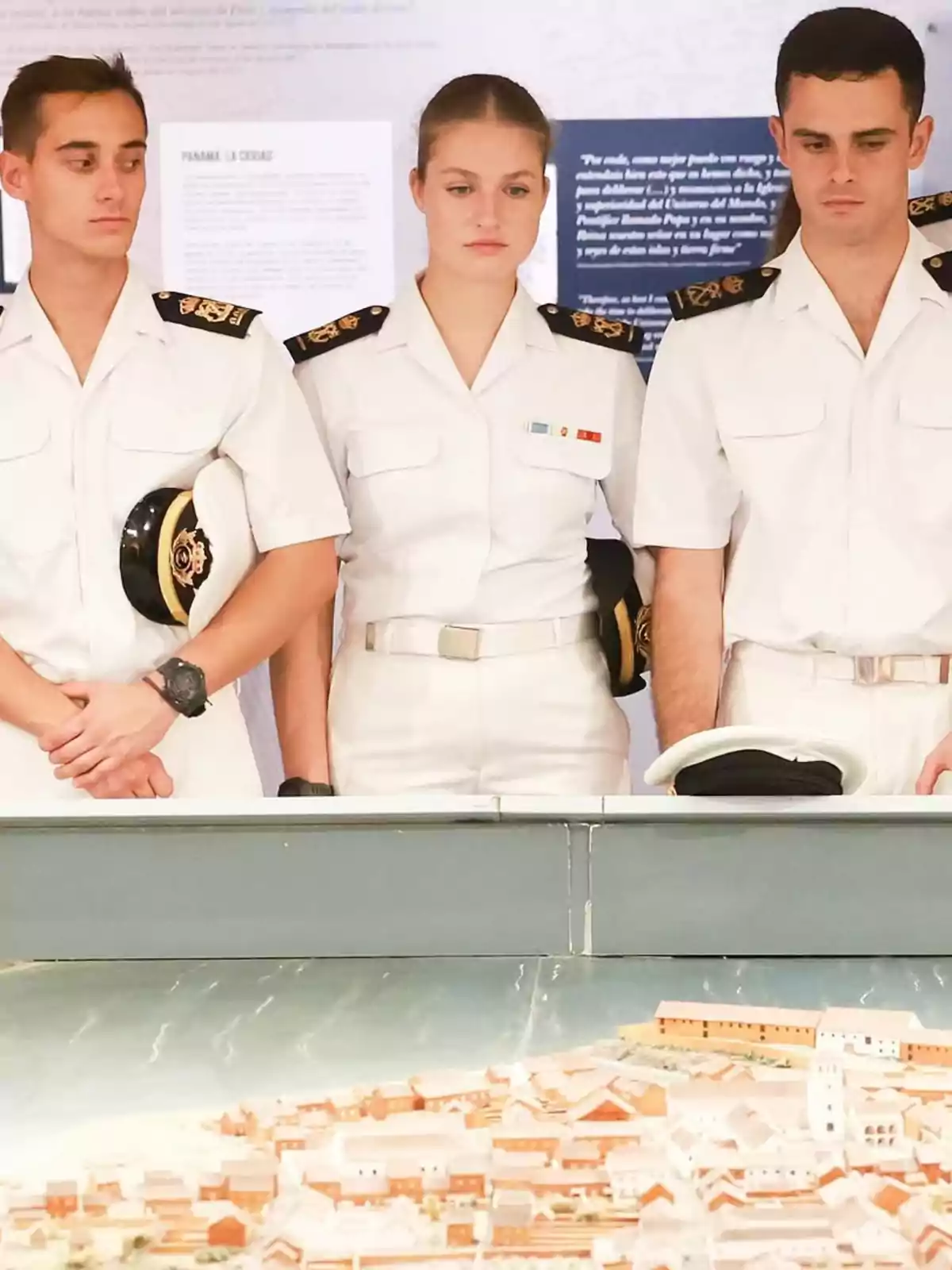 Tres personas vestidas con uniformes blancos de estilo naval observan un modelo a escala de una ciudad. Tres personas vestidas con uniformes blancos de estilo naval observan un modelo a escala de una ciudad.