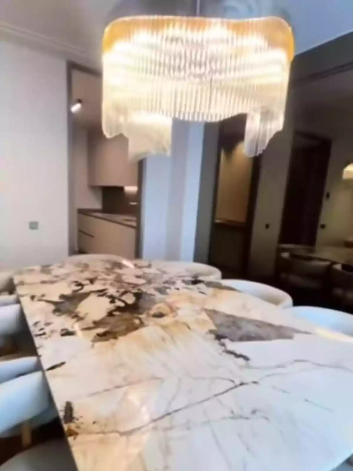 Mesa de mármol con vetas oscuras rodeada de sillas blancas bajo una lámpara colgante de diseño moderno en un comedor elegante Mesa de mármol con vetas oscuras rodeada de sillas blancas bajo una lámpara colgante de diseño moderno en un comedor elegante