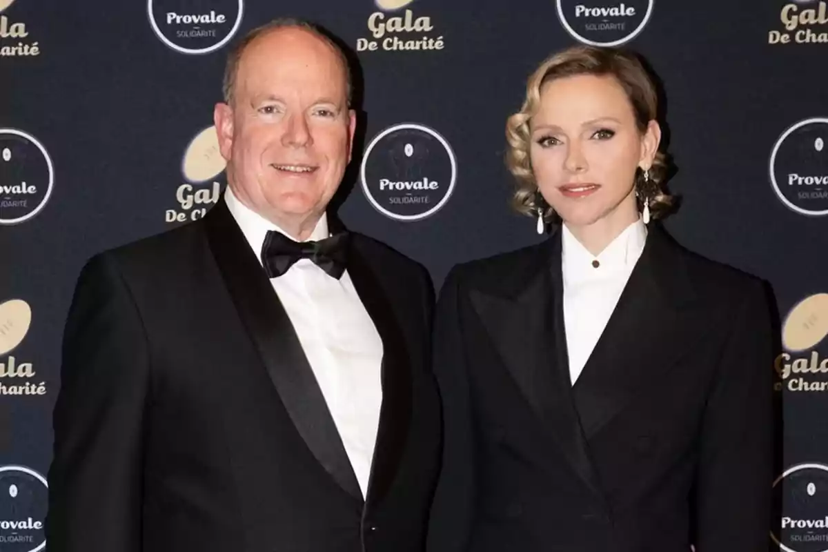 Alberto de Mónaco y Charlene elegantemente vestida posa en un evento de gala con un fondo que muestra logotipos de Alberto de Mónaco y Charlene elegantemente vestida posa en un evento de gala con un fondo que muestra logotipos de