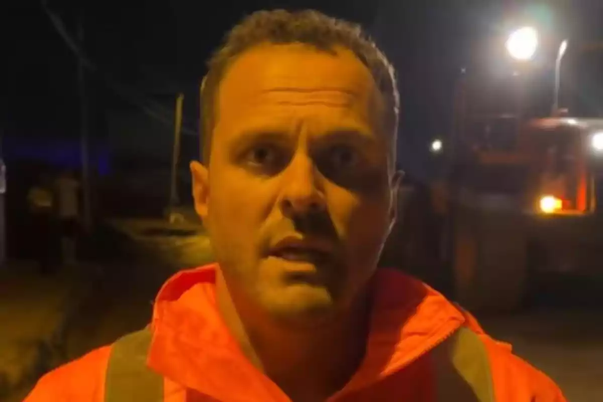 Yonathan de León con chaqueta naranja está de pie en una calle oscura iluminada por luces brillantes en el fondo. Yonathan de León con chaqueta naranja está de pie en una calle oscura iluminada por luces brillantes en el fondo.