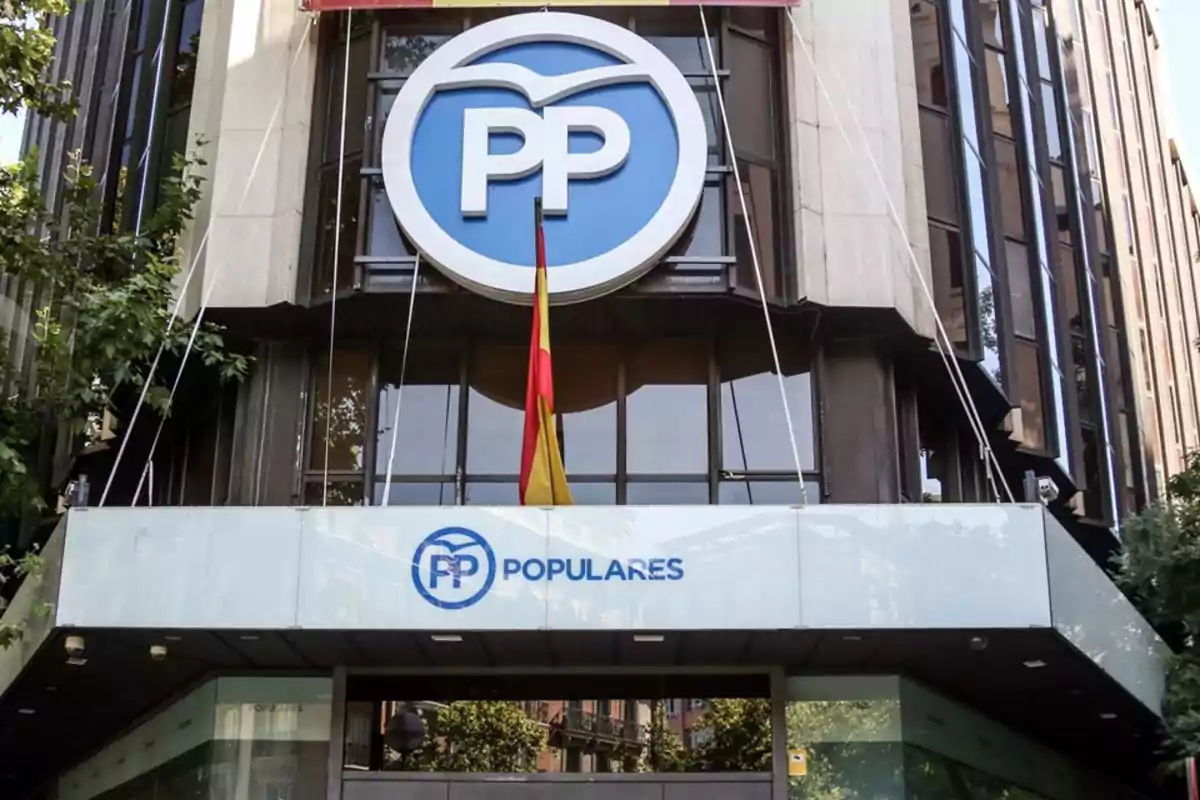 Edificio con logotipo azul y blanco de un partido político y una bandera española en la entrada. Edificio con logotipo azul y blanco de un partido político y una bandera española en la entrada.