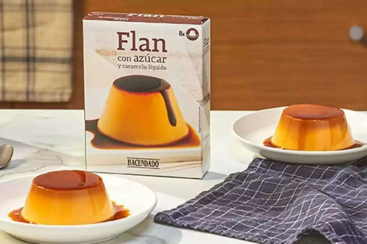 Caja de flan con azúcar y caramelo líquido de la marca Hacendado junto a dos porciones de flan servidas en platos blancos sobre una mesa con un paño azul. Caja de flan con azúcar y caramelo líquido de la marca Hacendado junto a dos porciones de flan servidas en platos blancos sobre una mesa con un paño azul.