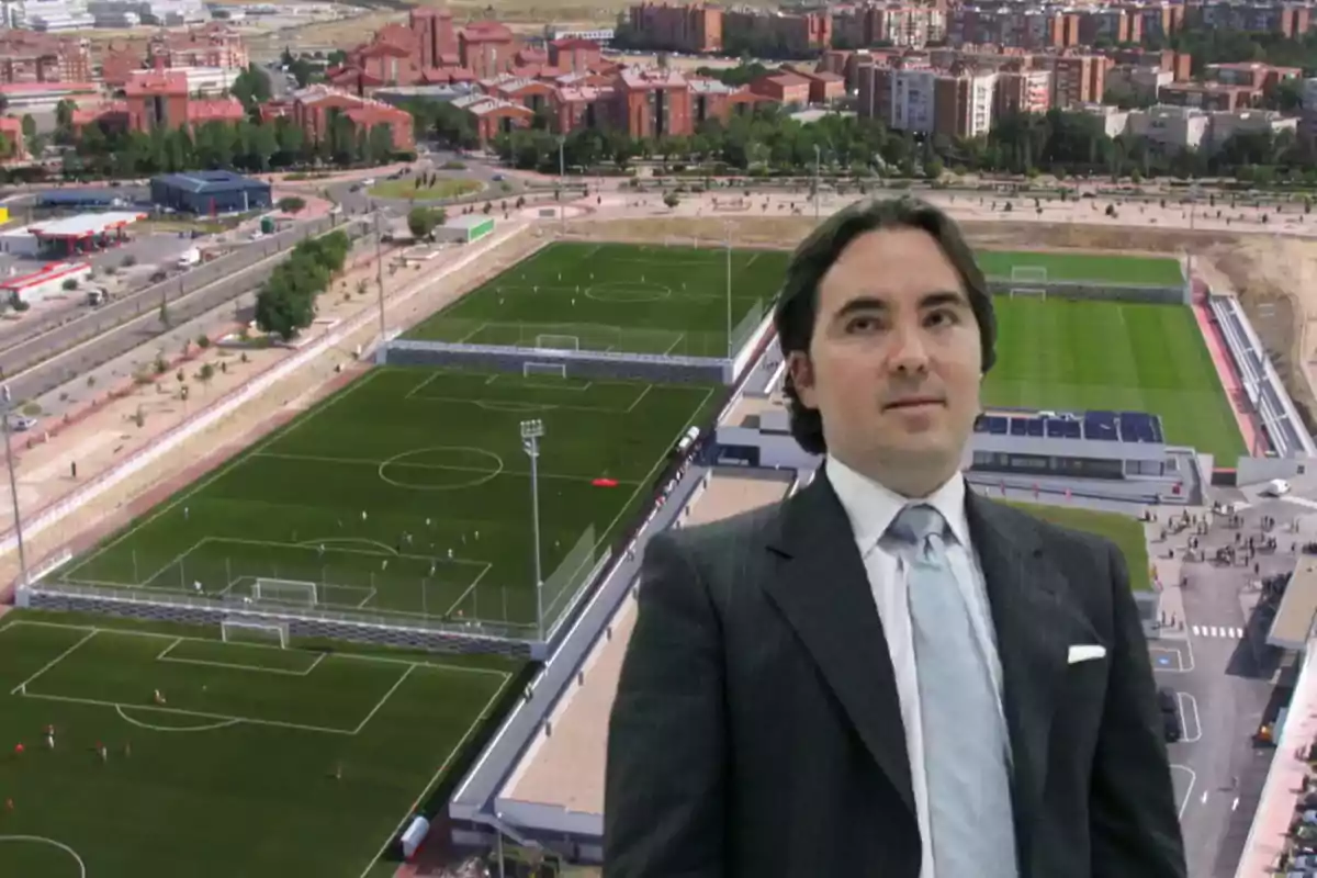 Un hombre con traje está superpuesto sobre una imagen aérea de un complejo deportivo con campos de fútbol y edificios residenciales al fondo.