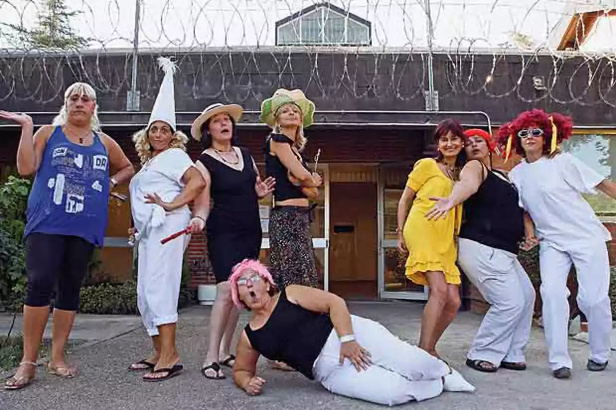Un grupo de mujeres disfrazadas posando de manera divertida frente a un edificio con alambre de púas en la parte superior Un grupo de mujeres disfrazadas posando de manera divertida frente a un edificio con alambre de púas en la parte superior