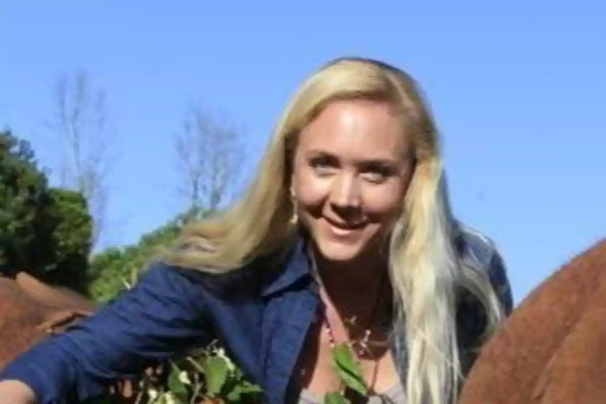 Mujer rubia sonriendo al aire libre con un cielo azul de fondo.