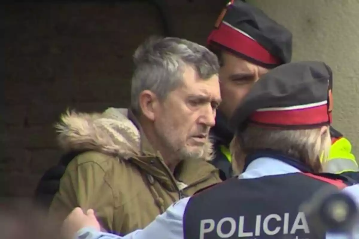 Un hombre es escoltado por dos policías que llevan uniformes con boinas rojas y negras.