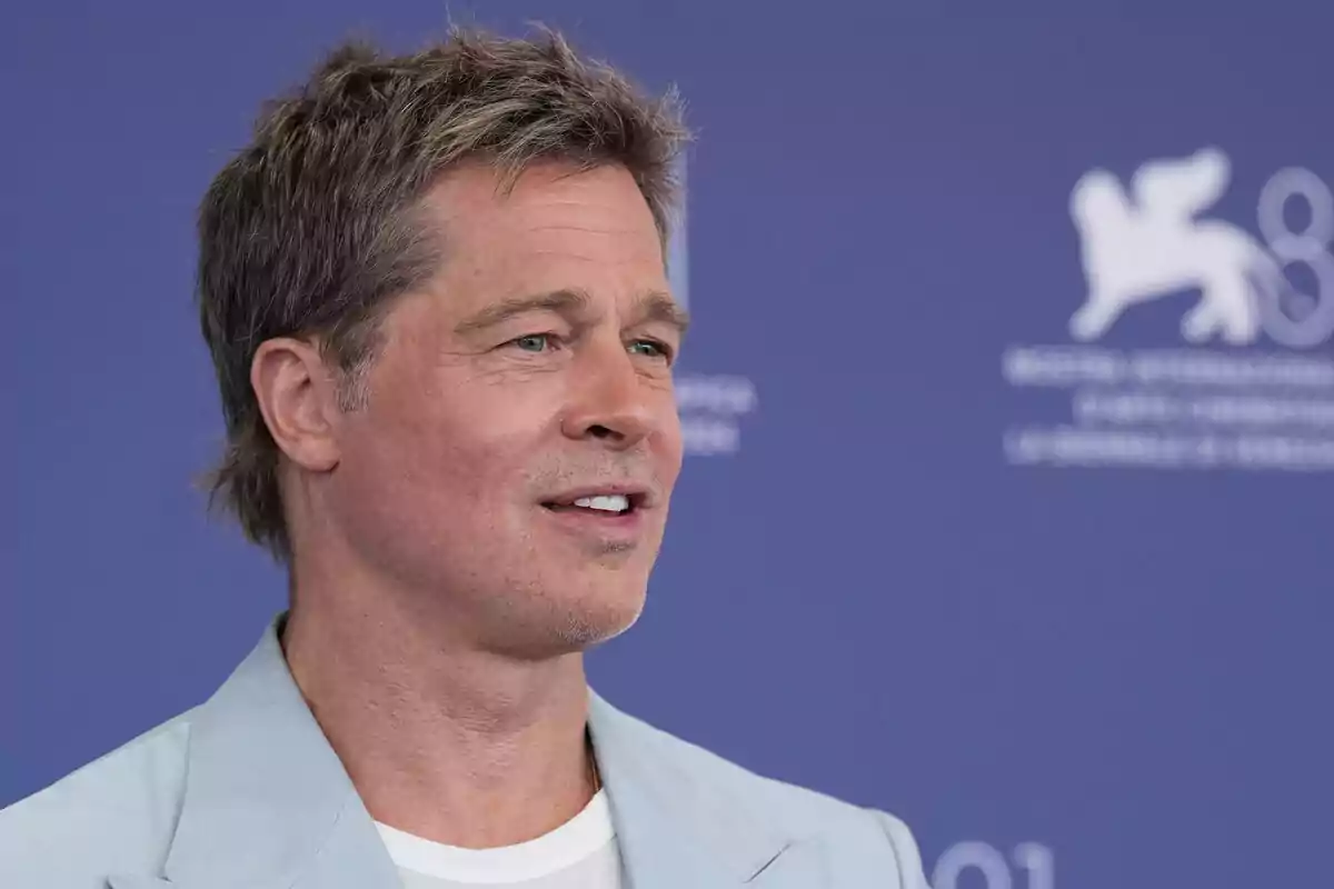 Brad Pitt con una chaqueta azul claro está sonriendo frente a un fondo azul con un logotipo blanco. Brad Pitt con una chaqueta azul claro está sonriendo frente a un fondo azul con un logotipo blanco.