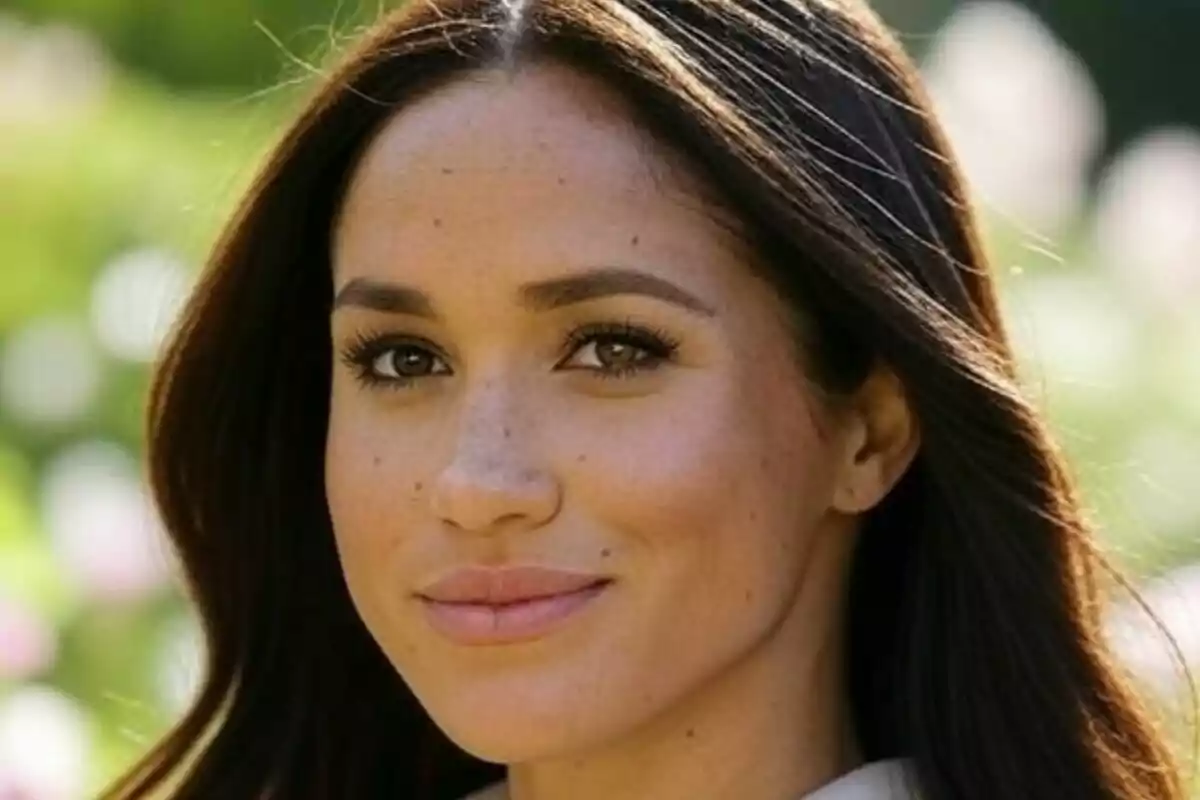 Primer plano de Meghan Markle mirando a la cámara en un entorno al aire libre y soleado.