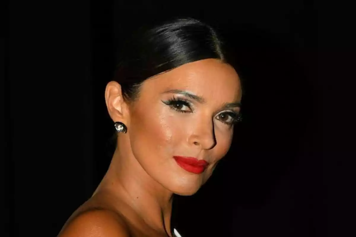 María Cerqueira con labios rojos y cabello oscuro recogido, usando aretes brillantes y fondo negro