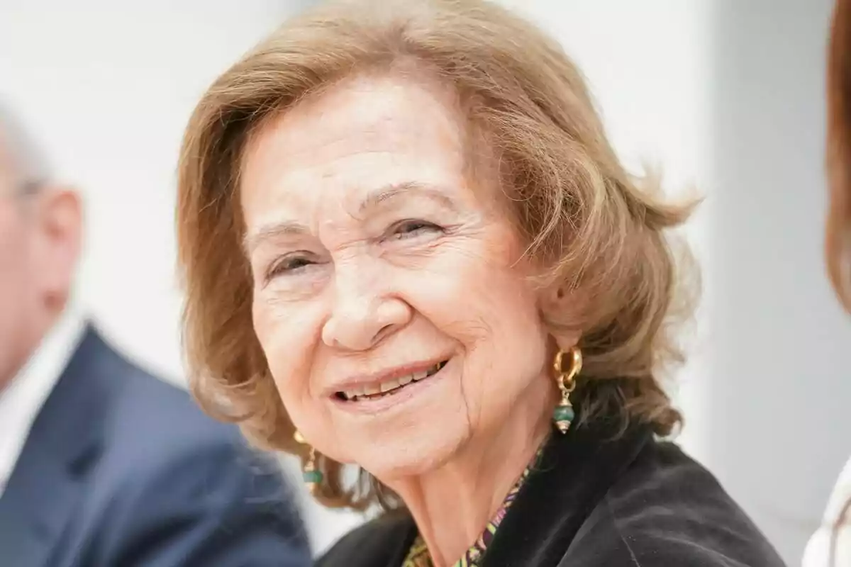 La reina Sofía sonriendo con el cabello castaño claro y pendientes dorados. La reina Sofía sonriendo con el cabello castaño claro y pendientes dorados.