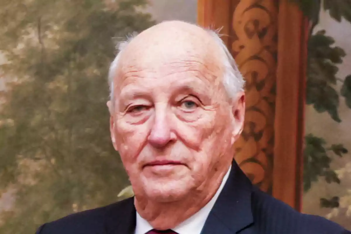 El rey Harald de Noruega con traje oscuro y corbata roja frente a un fondo decorativo. El rey Harald de Noruega con traje oscuro y corbata roja frente a un fondo decorativo.
