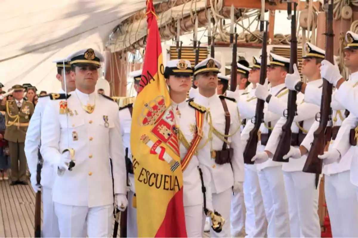 Grupo de oficiales navales en uniforme blanco sosteniendo una bandera y rifles durante una ceremonia en un barco. Grupo de oficiales navales en uniforme blanco sosteniendo una bandera y rifles durante una ceremonia en un barco.
