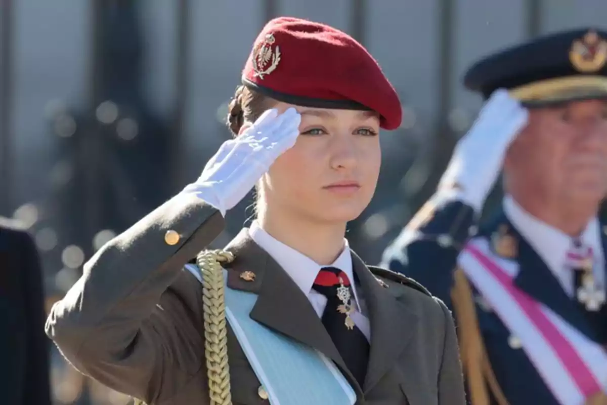 Una mujer soldado con boina roja y uniforme militar saluda durante una ceremonia oficial.