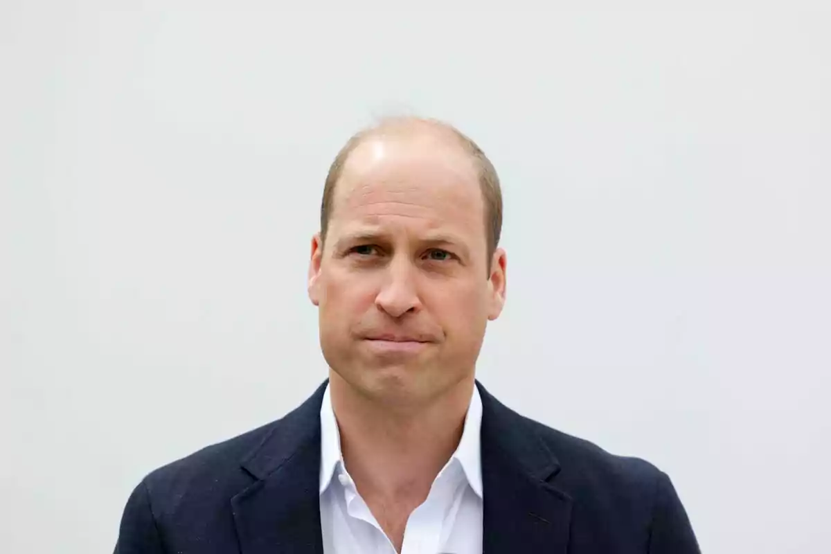 Prince William in a dark jacket and white jersey against a light background. Prince William in a dark jacket and white jersey against a light background.
