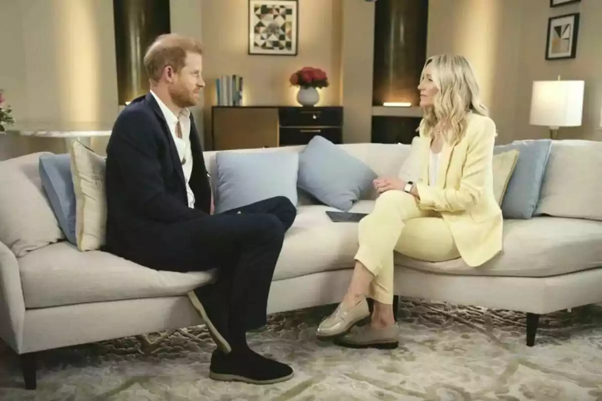 Príncipe Harry y periodista sentados en un sofá, Harry con traje oscuro y la otra con traje claro, conversando en un ambiente elegante y bien iluminado.