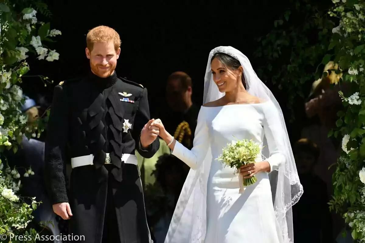 El príncipe Harry y Meghan Markle sonriente vestida de novios sale de un edificio decorado con flores. El príncipe Harry y Meghan Markle sonriente vestida de novios sale de un edificio decorado con flores.