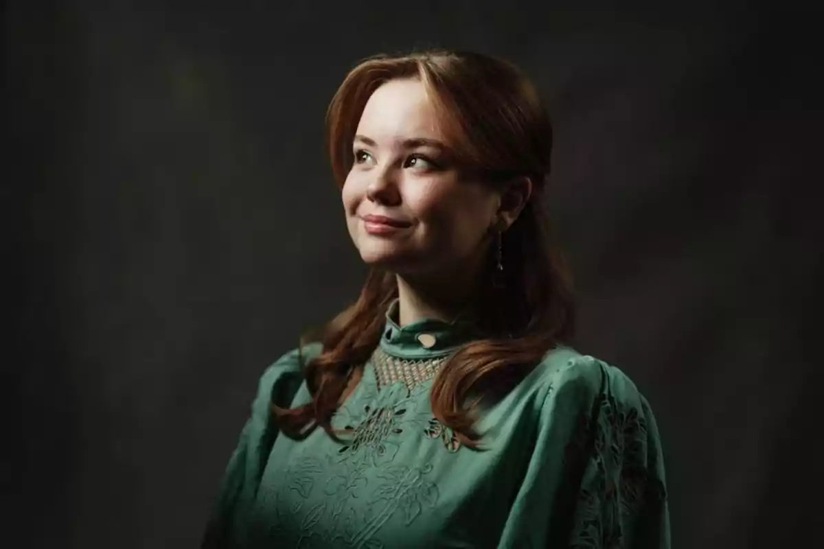 Una mujer joven con cabello castaño y suelto, lleva un vestido verde con detalles bordados y mira hacia arriba con una expresión serena. Una mujer joven con cabello castaño y suelto, lleva un vestido verde con detalles bordados y mira hacia arriba con una expresión serena.