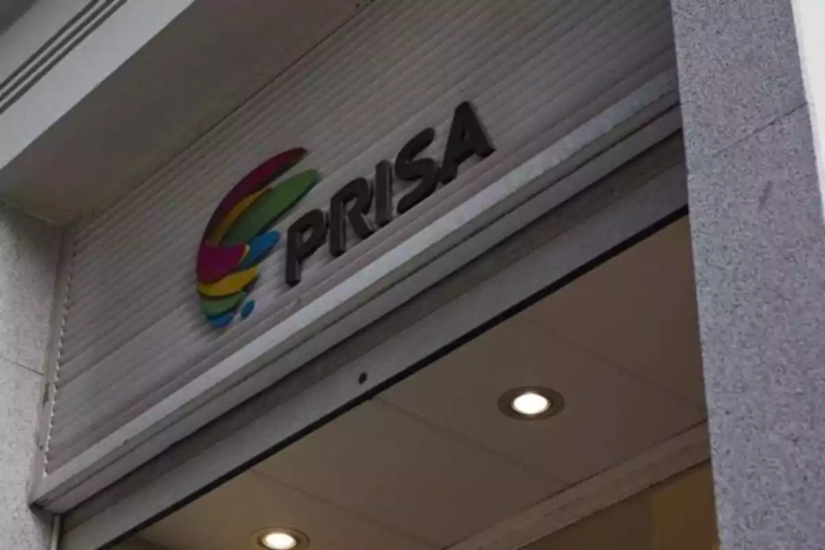 Fachada de un edificio con el logotipo de PRISA en letras negras y un diseño colorido al lado. Fachada de un edificio con el logotipo de PRISA en letras negras y un diseño colorido al lado.