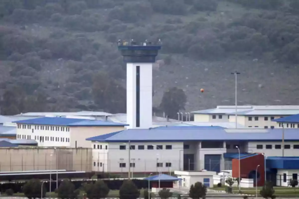 Vista de un complejo con edificios de techos azules y una torre de vigilancia en un entorno montañoso.