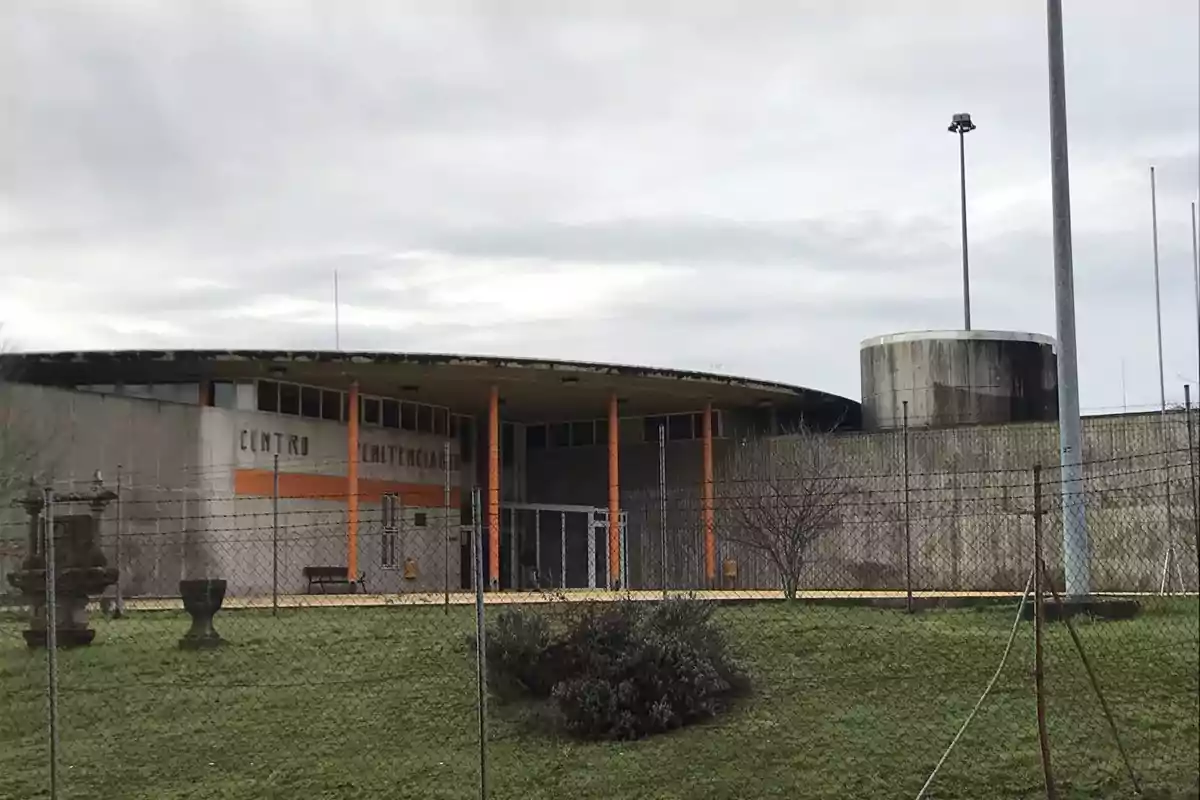 Edificio de un centro penitenciario rodeado de una cerca de alambre y un área verde en primer plano.