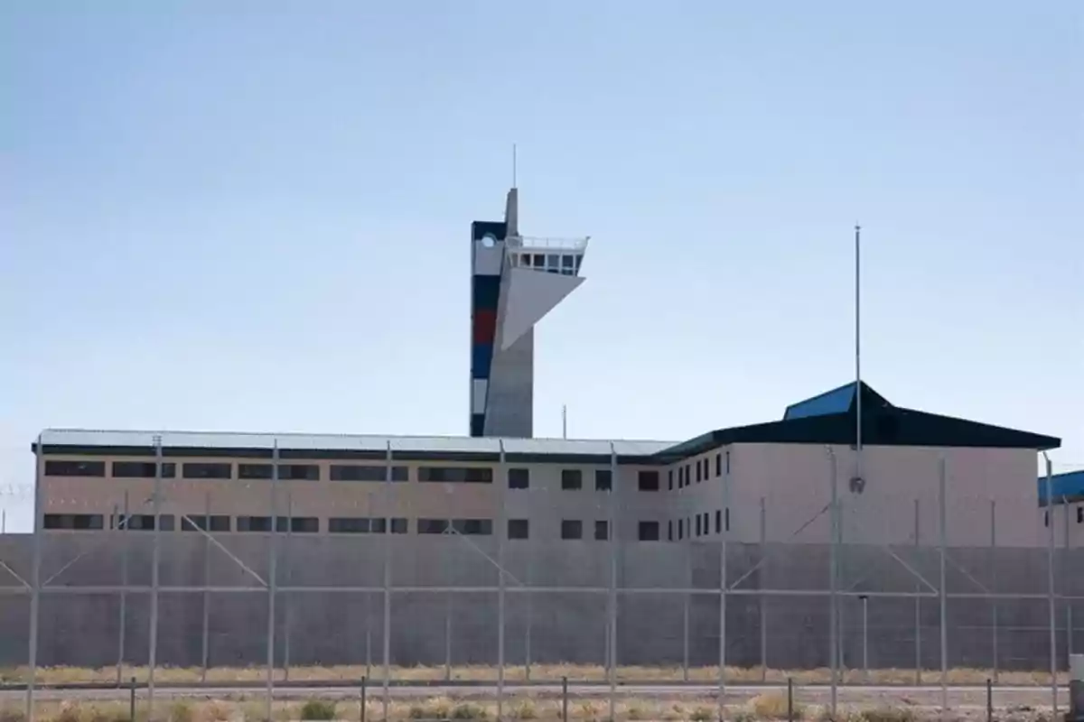 Edificio de una prisión con una torre de vigilancia y una cerca de alambre de púas en primer plano Edificio de una prisión con una torre de vigilancia y una cerca de alambre de púas en primer plano