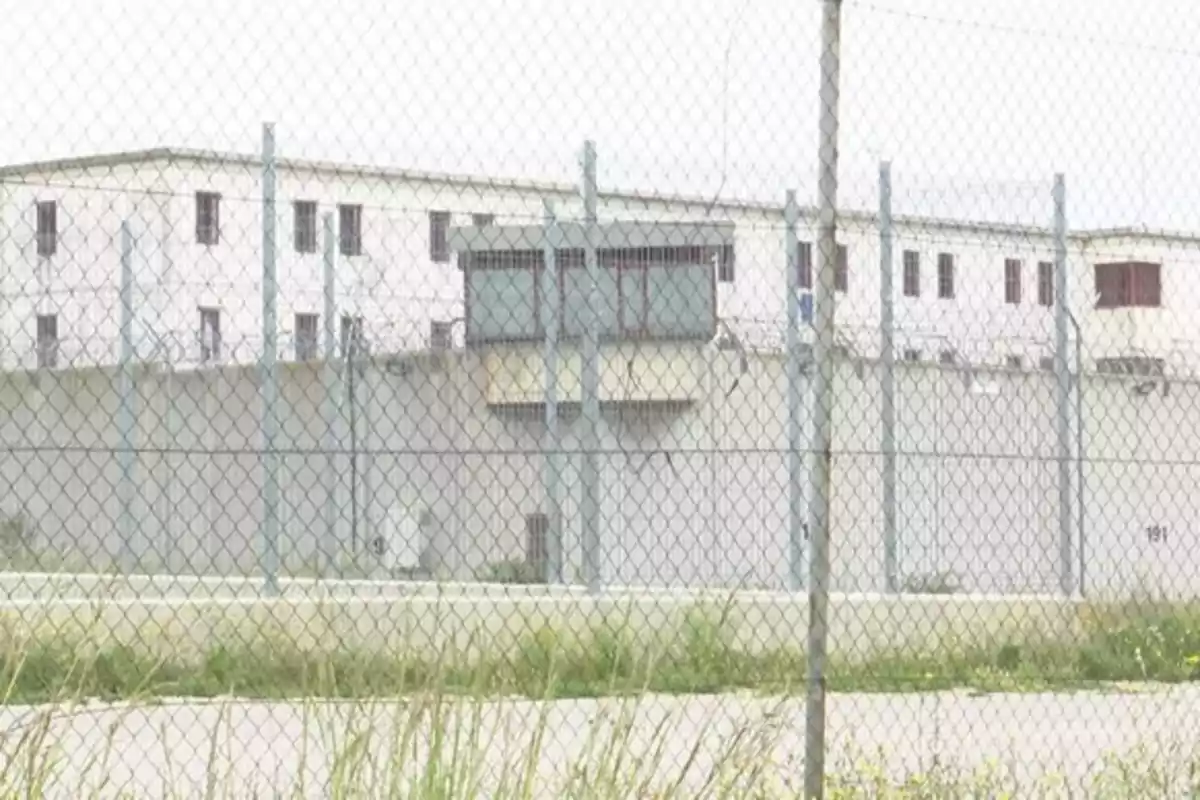 Edificio blanco rodeado de una cerca de alambre y vegetación en primer plano. Edificio blanco rodeado de una cerca de alambre y vegetación en primer plano.