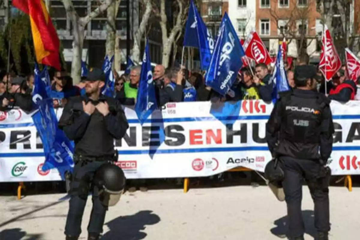 Manifestación con banderas y pancartas, vigilada por policías.