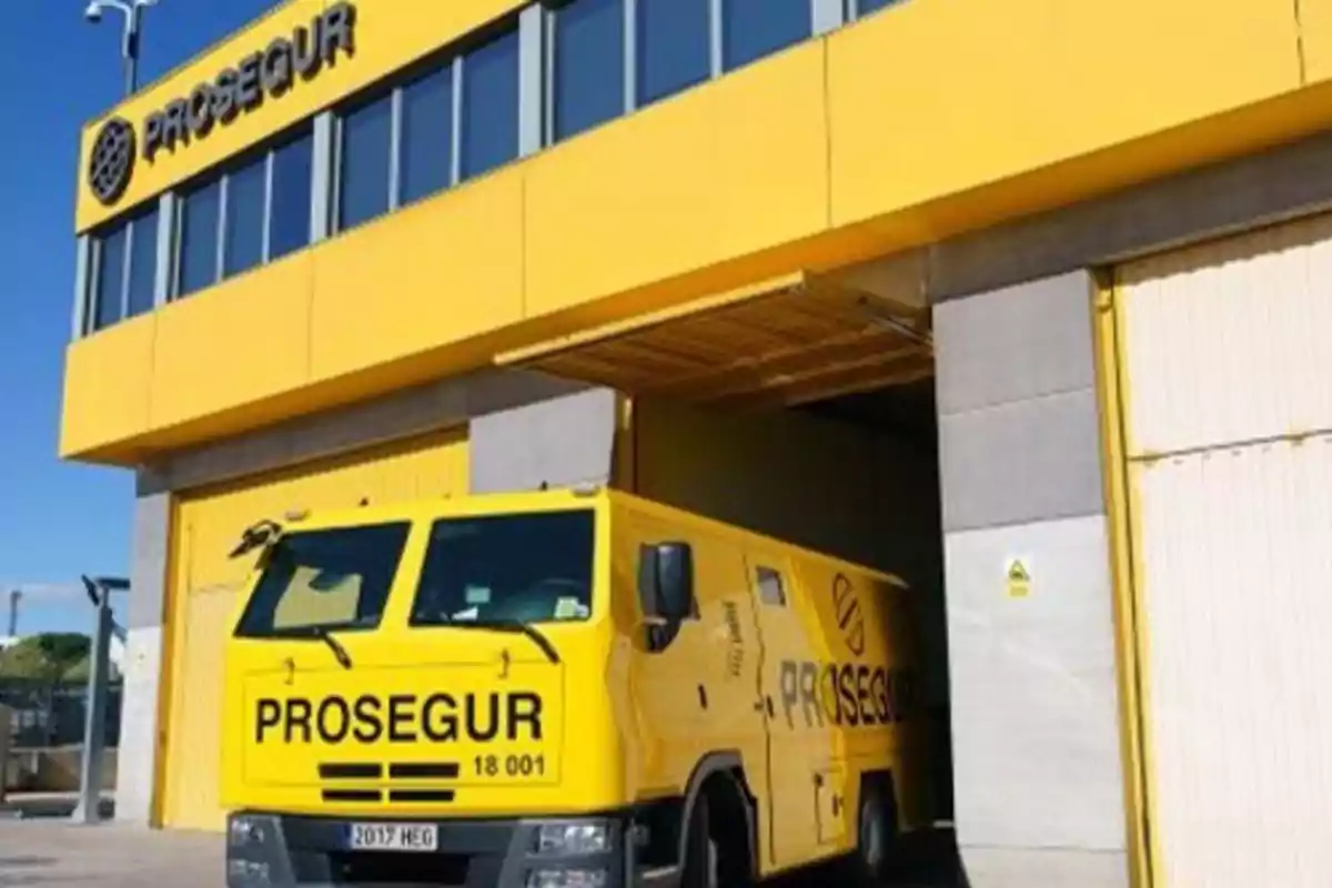 Un camión blindado amarillo de la empresa Prosegur saliendo de un edificio con el mismo nombre.