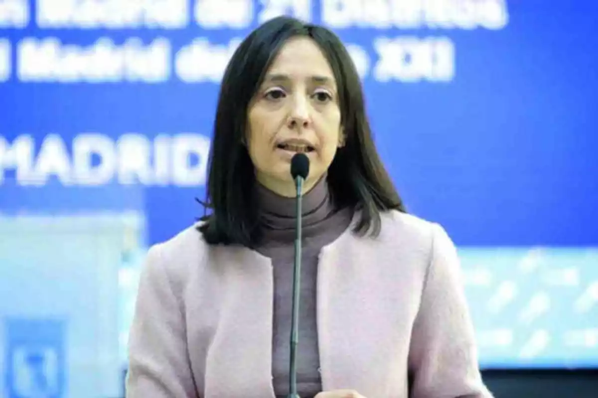 Una mujer hablando en un micrófono con un fondo azul que tiene texto borroso.