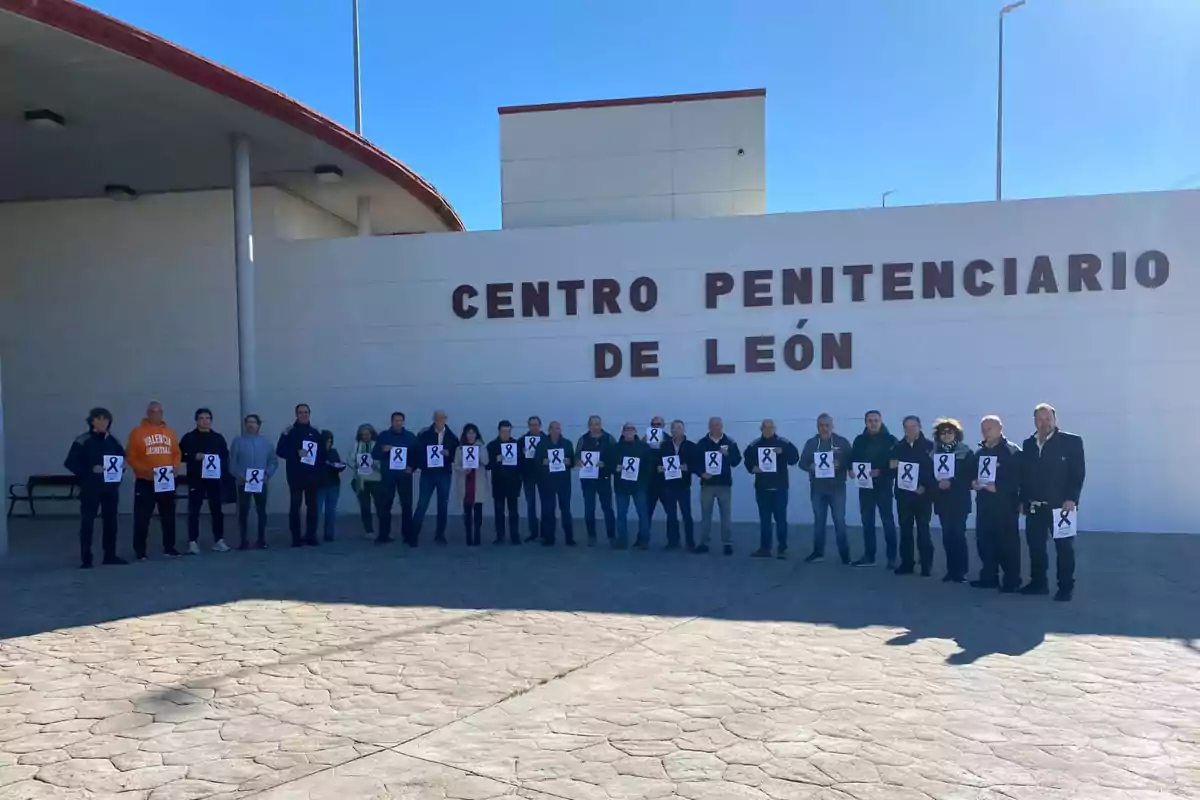 Un grupo de personas sostiene carteles con un lazo negro frente al edificio del Centro Penitenciario de León.