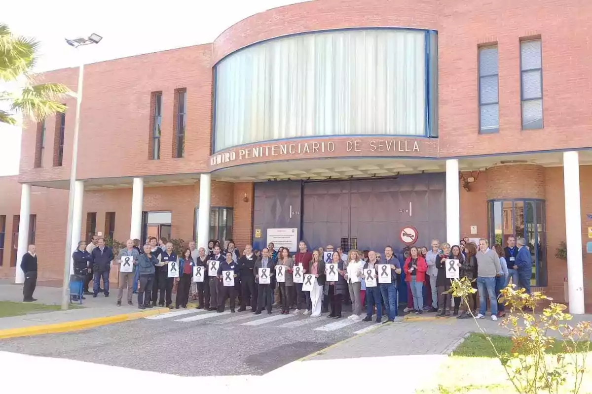 Un grupo de personas sostiene carteles con lazos negros frente al Centro Penitenciario de Sevilla.