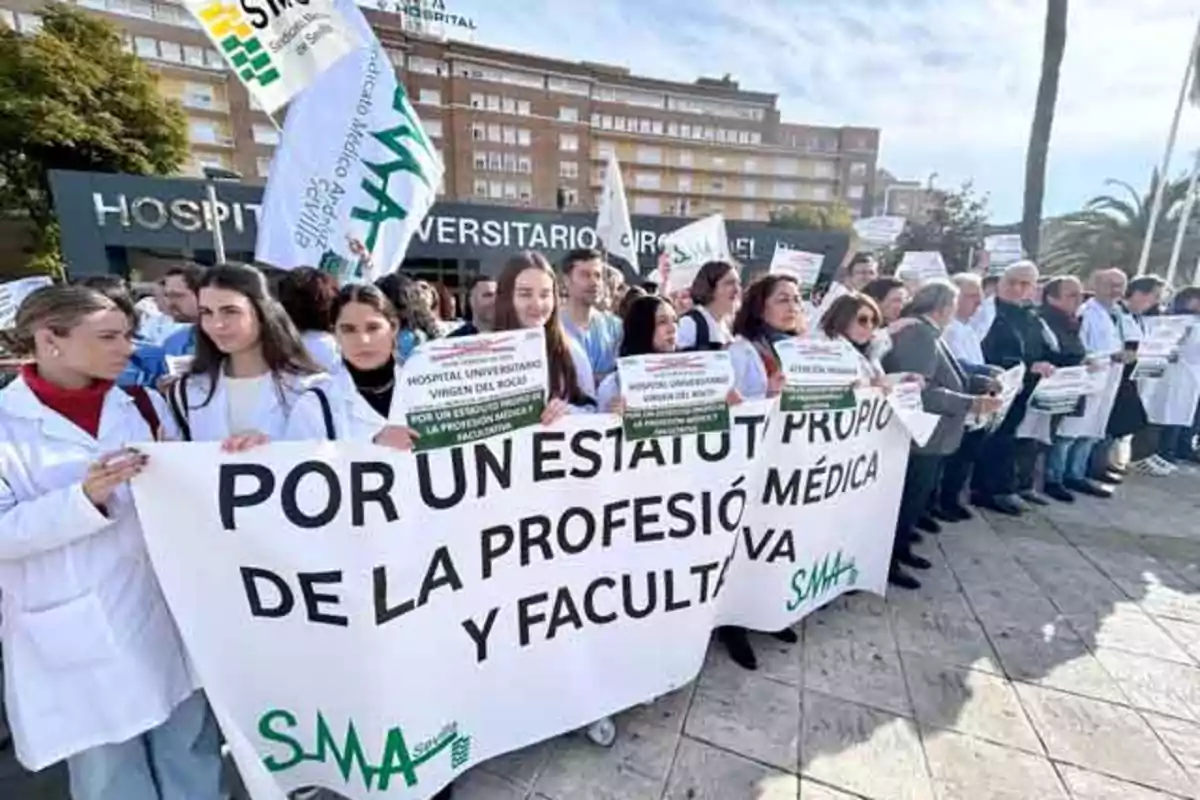 Un grupo de personas, muchas de ellas con batas blancas, sostiene pancartas y un cartel grande que dice "Por un estatuto propio de la profesión médica y facultativa" frente a un hospital.