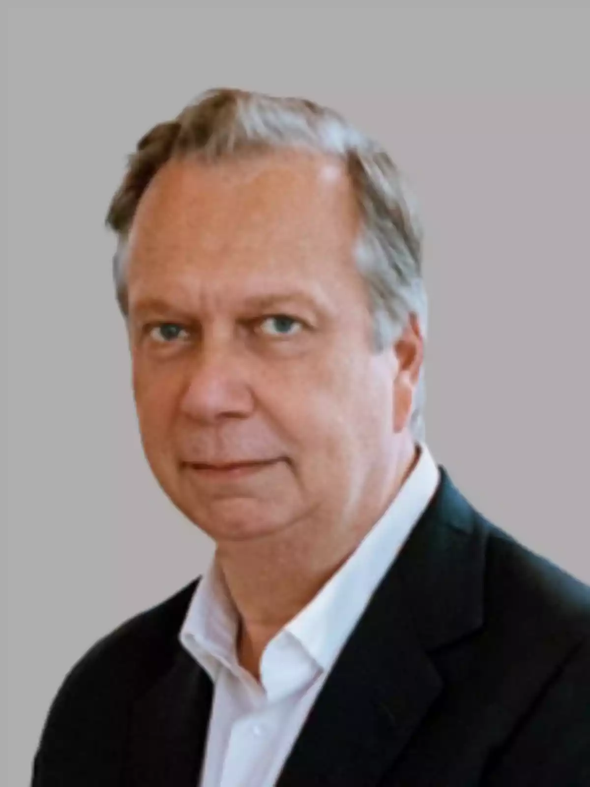 Un hombre de mediana edad con cabello canoso y expresión seria viste un traje oscuro y camisa blanca sobre un fondo gris. Un hombre de mediana edad con cabello canoso y expresión seria viste un traje oscuro y camisa blanca sobre un fondo gris.