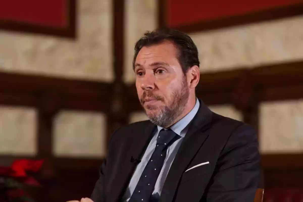 Hombre con traje oscuro y corbata azul en un entorno interior con paredes de madera y piedra. Hombre con traje oscuro y corbata azul en un entorno interior con paredes de madera y piedra.