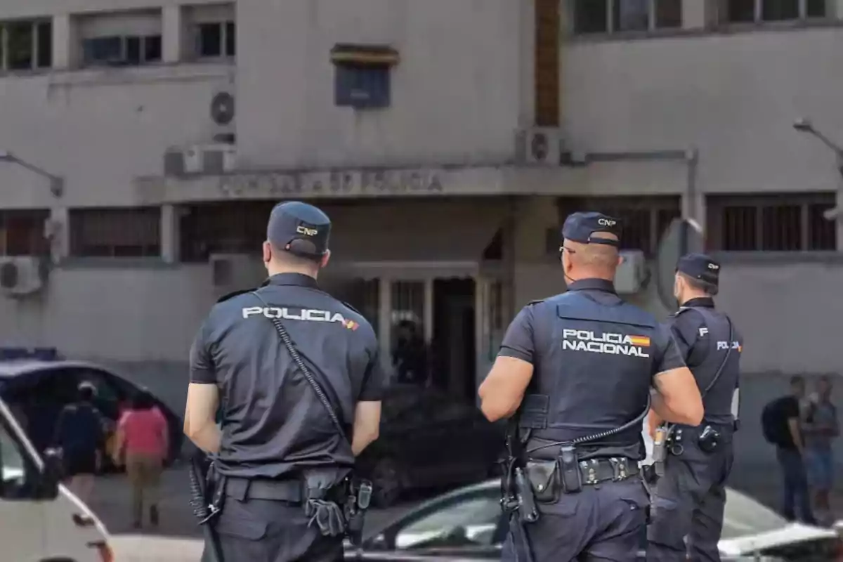 Tres agentes de la Policía Nacional de espaldas frente a un edificio de comisaría.